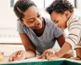 Eine Mutter zeigt ihrem Kind auf einem Buch, wann Kinder sprechen lernen.