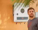Man tittar upp mot en Fronius Symo växelriktare på en orange vägg.