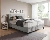 Sovrum med en stor säng i grått tyg. En fin balans att blanda beige och grått inredning med detaljer i trä och svarta tavlor på väggen.