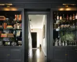 Estanterías oscuras con libros, botellas y copas. Ideas para como decorar una libreria con estilo y elegancia.