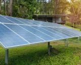 Grandes panneaux solaires au sol, installés dans un jardin verdoyant, captent l'énergie du soleil pour alimenter une maisonnette en bois.