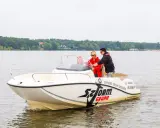 Trzy osoby na łodzi motorowej, jedna z nich uczy się sterować, zdobywając międzynarodowy patent sternika motorowodnego.