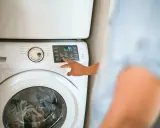 Dłoń naciska przycisk na panelu sterowania pralki, wybierając opcję "Eco Warm". Czy pralka sama podgrzewa wodę? Tak, ta opcja to umożliwia.