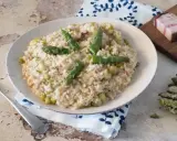 Un cremoso risotto con asparagi e pancetta, guarnito con punte di asparagi freschi e una spolverata di parmigiano.