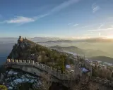 Un suggestivo viaggio a San Marino: torri medievali su un crinale roccioso, con la nebbia che avvolge le valli sottostanti al tramonto.