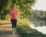 Frau genießt ihr Lauftraining am See. Nach 1 Monat Joggen fühlt sie sich fitter und strahlt Selbstvertrauen aus.
