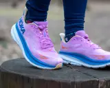 Fioletowe buty Hoka Clifton na pniu drzewa. Hoka to firma znana z amortyzacji.