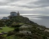 Leuchtturm und Gebäude auf felsiger Küste bei Finisterre, Spanien. Grauer Himmel über dem Meer.