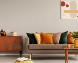Un salon cosy aux couleurs automnales, avec un canapé garni de coussins ocre et vert forêt, un meuble vintage en bois et une peinture abstraite.