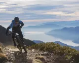 Ein Mountainbiker auf einer abenteuerlichen Tour in den Alpen, mit einem See und Bergketten im Hintergrund.