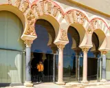 Verzierte Bögen und Säulen der Medina Azahara spiegeln sich in Glas. Besucher bestaunen die historische Architektur.