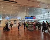 Ludzie w terminalu lotniska, tablice z informacjami o bramkach i pasażerowie z bagażami.