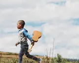 Kleines Kind, 17 Monate, sehr anstrengend, rennt mit Ukulele über Feld.