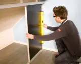 Un homme utilise un niveau pour fabriquer un placard sous pente de toit.