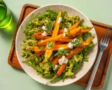 Un plat de pâtes vertes garni de carottes rôties et de fromage frais, avec des fanes de carottes pour la décoration.