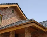Nowy dom z cegły, z drewnianą deską czołową i brązowym rynnowym systemem.