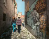 Coppia passeggia in un vicolo di Saludecio, ammirando un murale. Scopri cosa vedere in questo borgo incantevole.