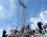 Grupa turystów na skalistym szczycie pod wysoką, metalową konstrukcją krzyża.