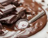 Morceaux de chocolat noir fondus, un thermomètre indiquant 31°C, parfait pour le temperage chocolat au lait.
