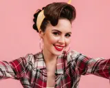 Uśmiechnięta dziewczyna w stylu pin up, z burzą brązowych włosów upiętych w kok i żółtą bandanką, w kraciastą koszulę.