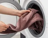 Manos colocando una toalla rosa en una lavadora. Aprende como lavar toallas para que queden suaves y esponjosas.