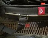 Czerwona metka z logo **Vaude** na czarnym plecaku. Firma Vaude to niemiecki producent sprzętu turystycznego.