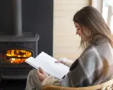 Une femme lit un livre près d'un poêle à granulés sans électricité. Avis : chaleur réconfortante et ambiance cosy.