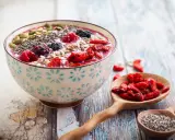 Miseczka smoothie z owocami, nasionami chia, pestkami dyni i słonecznika. Obok łyżka z jagodami goji. Nasiona chia jak jeść? Dodaj do smoothie!