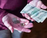 Dłonie trzymające polskie banknoty i monety. Zastanawiasz się, ile wynosi dodatek do emerytury za warunki szkodliwe?