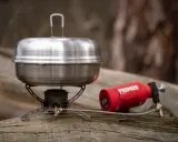 En primus kaffepanna på en campingkök med en röd gasbehållare. Perfekt för fika i naturen.