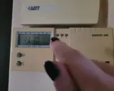 Dłoń z czarnym lakierem na paznokciach dotyka termostatu, sterowanie piecem gazowym. Na wyświetlaczu 13:10 i 17.5°C.
