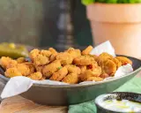 Knusprig frittierte Gurkenscheiben, **fried pickles**, in einer Schale, daneben ein Dip und ganze Gewürzgurken.