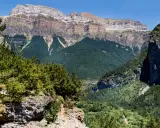 Paisaje de Ordesa y Monte Perdido con niños explorando senderos entre bosques frondosos y imponentes montañas.