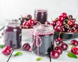 Słoiki z dżemem wiśniowym i świeże wiśnie na drewnianym stole. Idealne, by pokazać, co zrobić z wiśni.