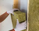 Manos enguantadas colocan aislamiento de lana de roca para como aislar una pared, creando un hogar más cálido y eficiente.