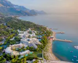 Widok z lotu ptaka na Rixos Sungate, luksusowy kurort nad turkusowym morzem, otoczony zielenią i górami.