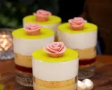 Fyra små prinsesstårta i glas, dekorerade med rosa marsipanrosor och gul marsipanlock. Vackert uppdukat med ljus i bakgrunden.