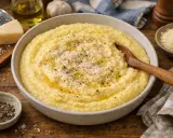 Polenta crémeuse dans un bol, garnie de parmesan râpé et de poivre noir, avec une cuillère en bois.