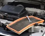 W silniku samochodu leży brudny filtr powietrza, gotowy do wymiany. Klucz leży na filtrze, wskazując, gdzie jest filtr powietrza.
