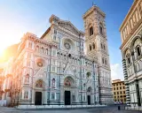 La majestueuse coupole de Florence, le Duomo, se dresse fièrement sous un ciel bleu, baignée par les rayons du soleil.