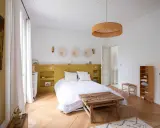 Une chambre lumineuse avec une tête de lit peinture jaune moutarde, des décorations murales en paille et un lit blanc douillet.