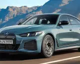 Der neue BMW i4 Facelift in einem eleganten Blau fährt auf einer Küstenstraße vor einer Bergkulisse.