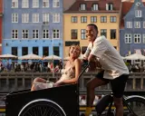 Ett par njuter av en romantisk weekend i Europa, cyklar längs en kanal med färgglada hus i bakgrunden.
