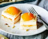 Zwei exquisite Stücke spiegeleikuchen mit pudding, garniert mit Pfirsich und Pistazien, auf einem Teller mit einer Gabel.