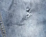 Jak zaszyć dziurę w spodniach dresowych? Widok z bliska na przetarty jeans z widocznym uszkodzeniem, które można naprawić.