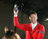 Reiter Franke Sloothaak hält stolz seinen Helm hoch, trägt eine rote Reitjacke und sitzt auf einem braunen Pferd.