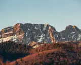 Skały Giewontu, ośnieżone i oświetlone słońcem, wznoszą się nad lasem. Choć trudno określić jaką wysokość ma Giewont, jego majestat robi wrażenie.