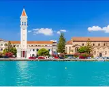 Widok na miasto Zakynthos z turkusową wodą i budynkami, w tym kościołem z charakterystyczną wieżą.
