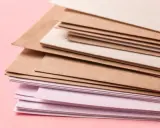 Stos papierów w różnych odcieniach brązu i różu. Różne rodzaje papieru, od kraftowego po delikatnie barwiony, tworzą ciekawą kompozycję.