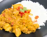Pyszny kurczak curry z ryżem, udekorowany papryką i natką kolendry, podany na czarnym talerzu.